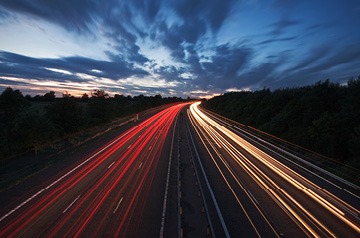 Headlights and brake lights rushing along a divided highway under a cloud-filled dawn sky